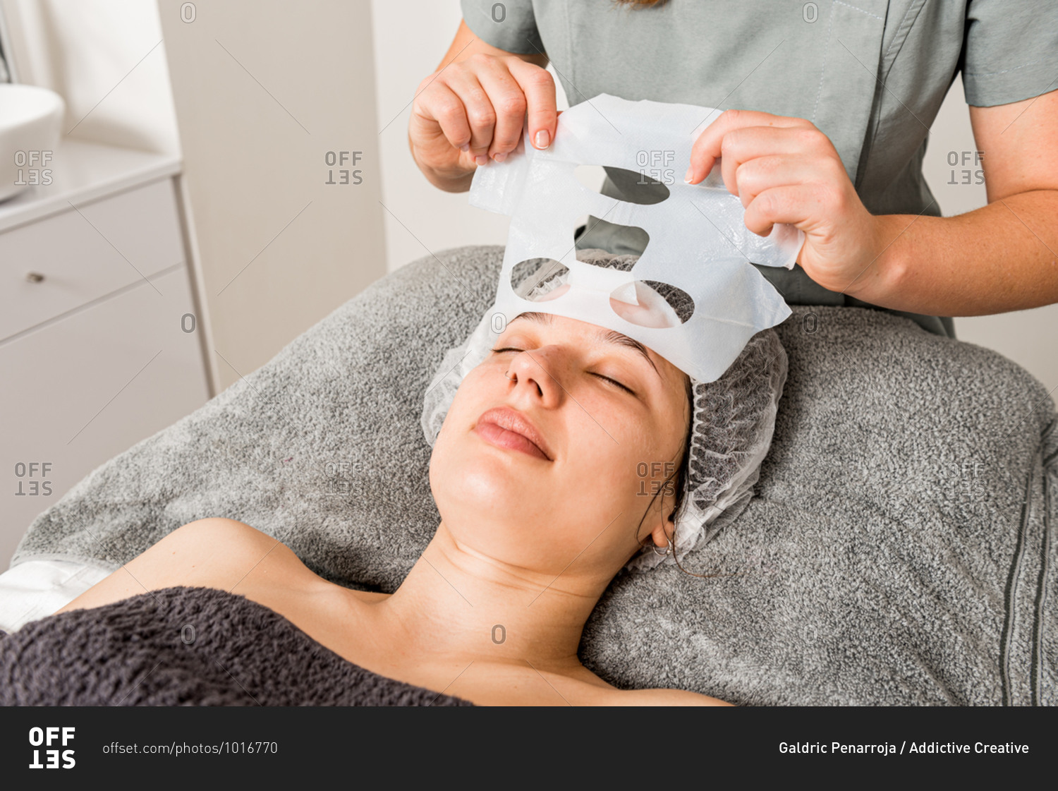 Crop unrecognizable beautician removing moisturizing cloth mask from face of relaxed female client during professional treatment in modern clinic