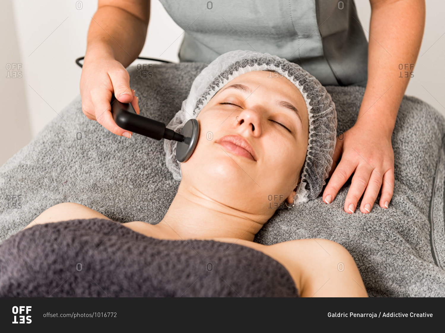 Relaxed female client getting skincare facial massage with ultrasound device from cropped unrecognizable professional cosmetician in contemporary beauty clinic