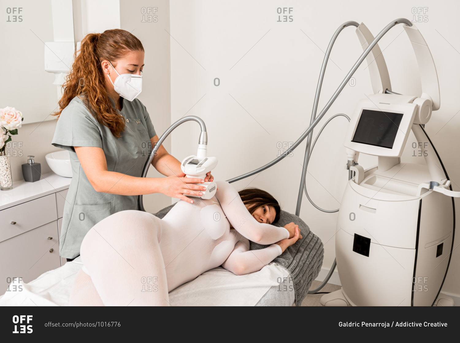 Masseuse in protective mask doing anti cellulite lipo massage to female client arm dressed in white suit during body care procedure in salon of apparatus cosmetology