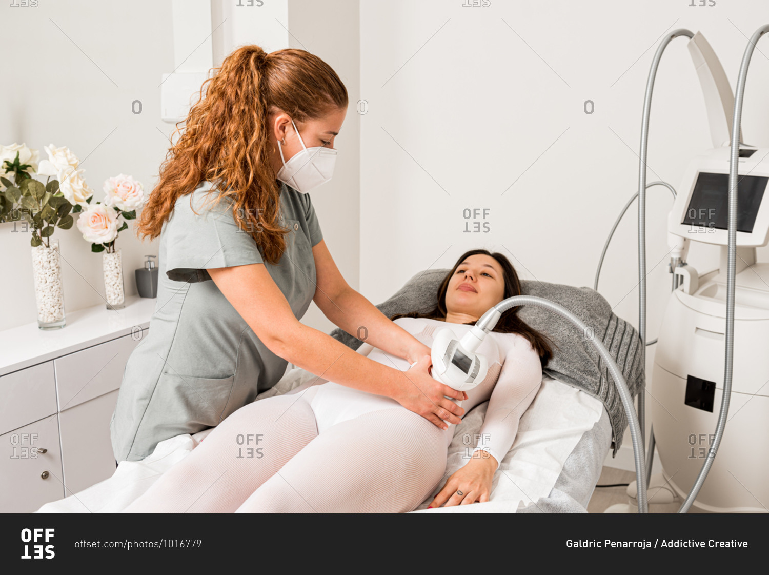 Masseuse in protective mask doing anti cellulite lipo massage to female client waist dressed in white suit during body care procedure in salon of apparatus cosmetology
