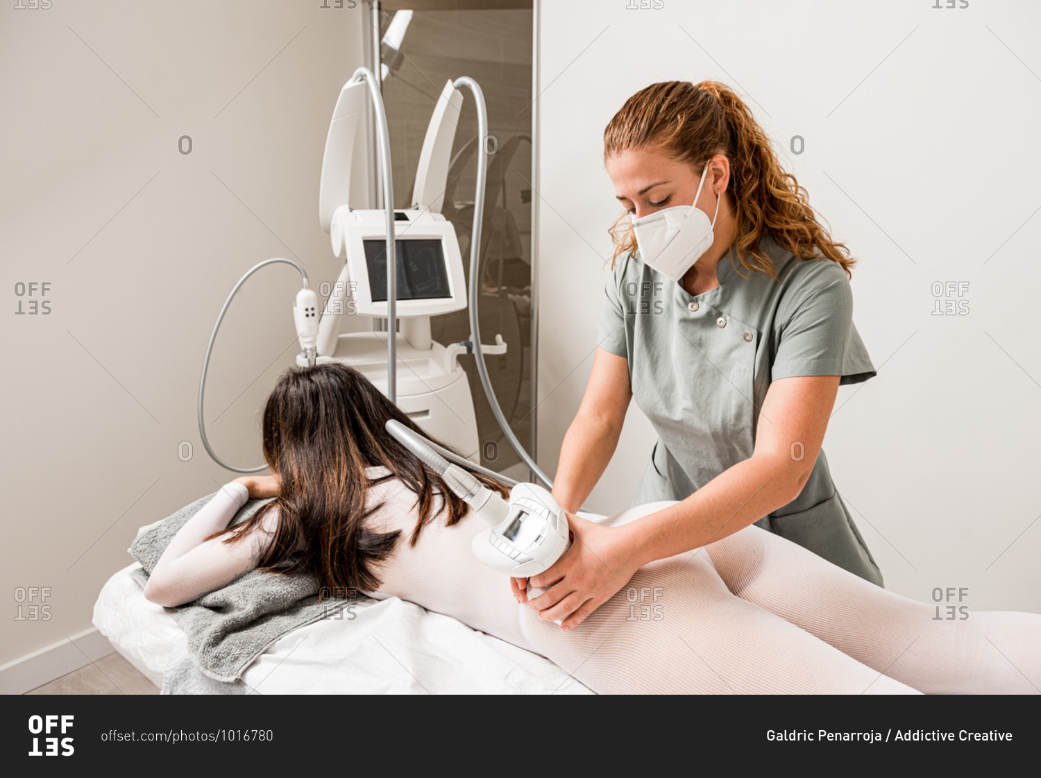 Masseuse in protective mask doing anti cellulite lipo massage to female client buttocks dressed in white suit during body care procedure in salon of apparatus cosmetology