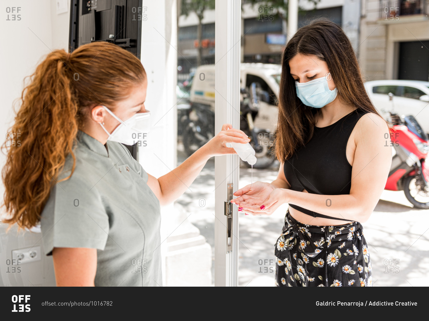 Staff of modern beauty salon applying sanitizer for disinfection to hands of young female customer in protective mask before entering office