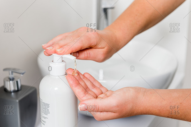 Crop anonymous female pressing dispenser with sanitizer gel placed on counter near sink