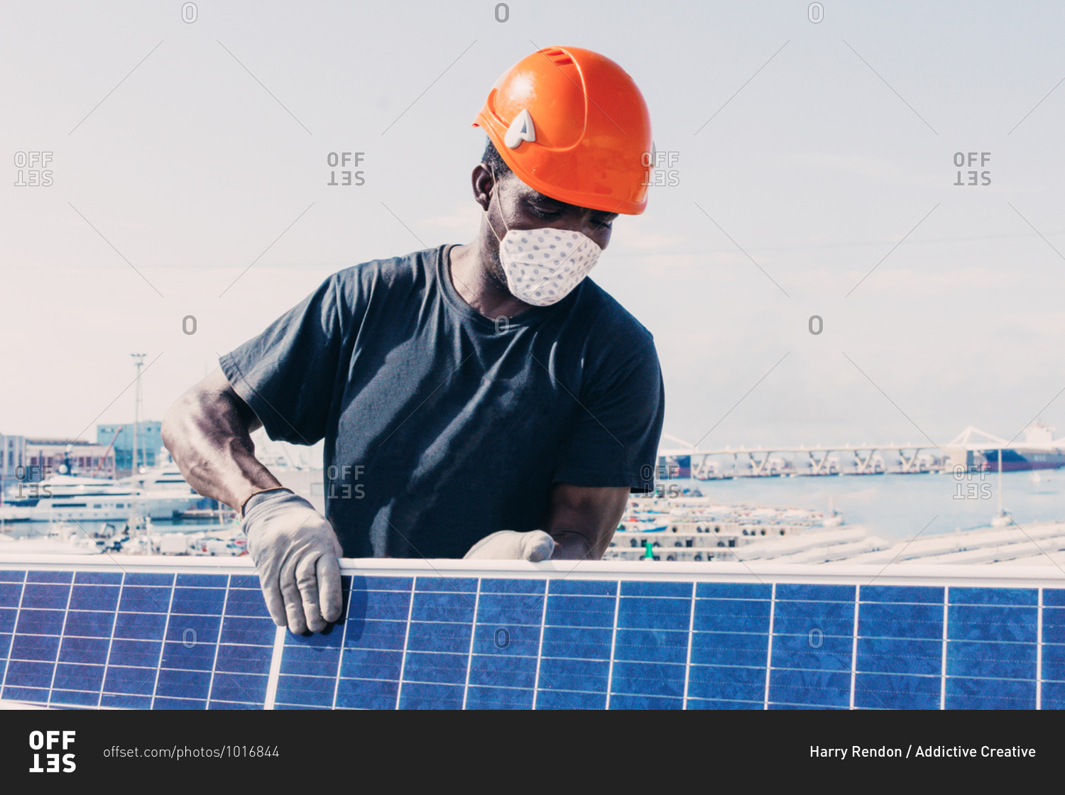 Black workman in helmet and protective mask installing solar battery in industrial area of contemporary plant