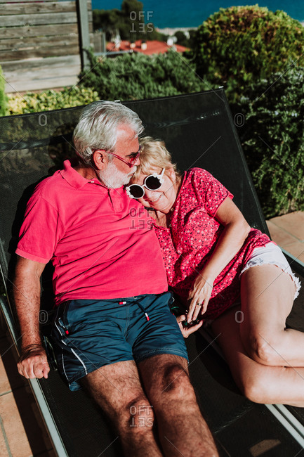 Tender elderly couple lying on deck chairs and resting together at resort during summer vacation on sunny day