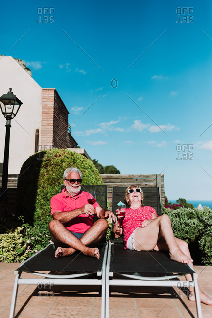High angle of relaxed senior couple lying on loungers on terrace and drinking refreshing tropical cocktails while enjoying summer holiday