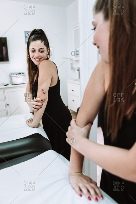 Satisfied young female client standing near mirror and examining new tattoo on arm in modern salon