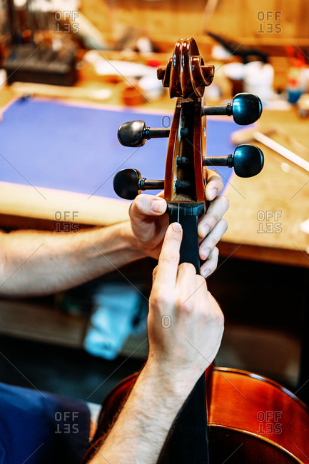 Closeup of violin peg box in hands of anonymous luthier during process of repairing and tuning instrument in workshop