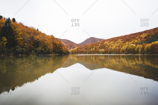 Peaceful landscape of calm lake surrounded by orange trees of Irati Forest in Navarra