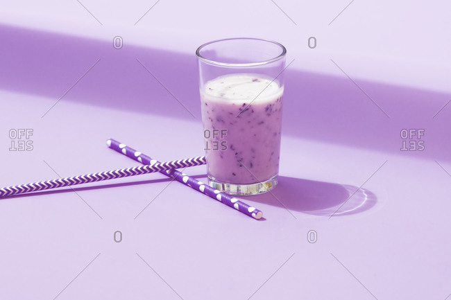 Glass of yummy cold natural blueberry smoothie placed with straw on lilac table