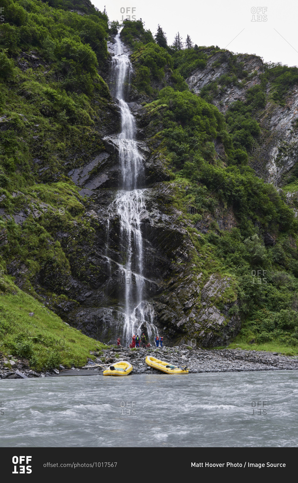 Group of adventure tourists looking at mountain waterfall on river bank, Valdez, Alaska, USA
