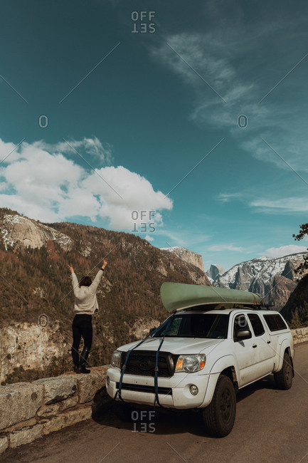 Young woman on top of roadside wall with hands raised, rear view, Yosemite Village, California, USA