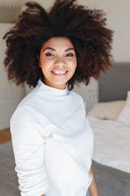 Happy young woman with afro hairstyle in bedroom, waist up portrait
