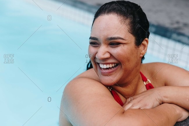 Mid adult woman with wet hair leaning on outdoor swimming poolside, looking over her shoulder, Cape Town, South Africa