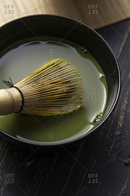 Still life of matcha tea preparation with whisk in bowl of matcha tea, close up, overhead view