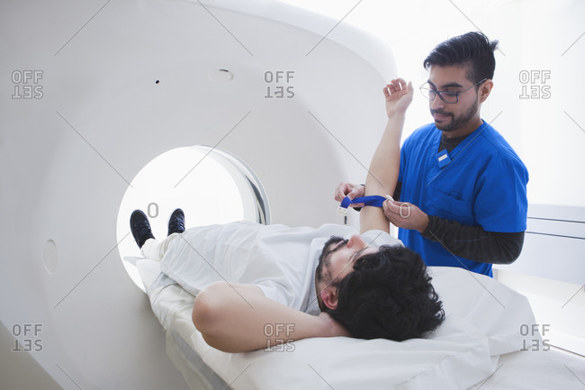 Young male radiographer preparing male patient for CT scan in radiology department