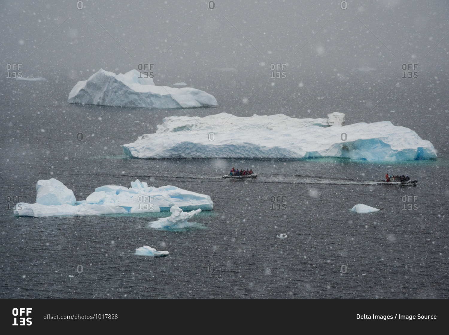 Tourists in inflatable boat sailing past icebergs in snowstorm, Portal Point, Antarctica