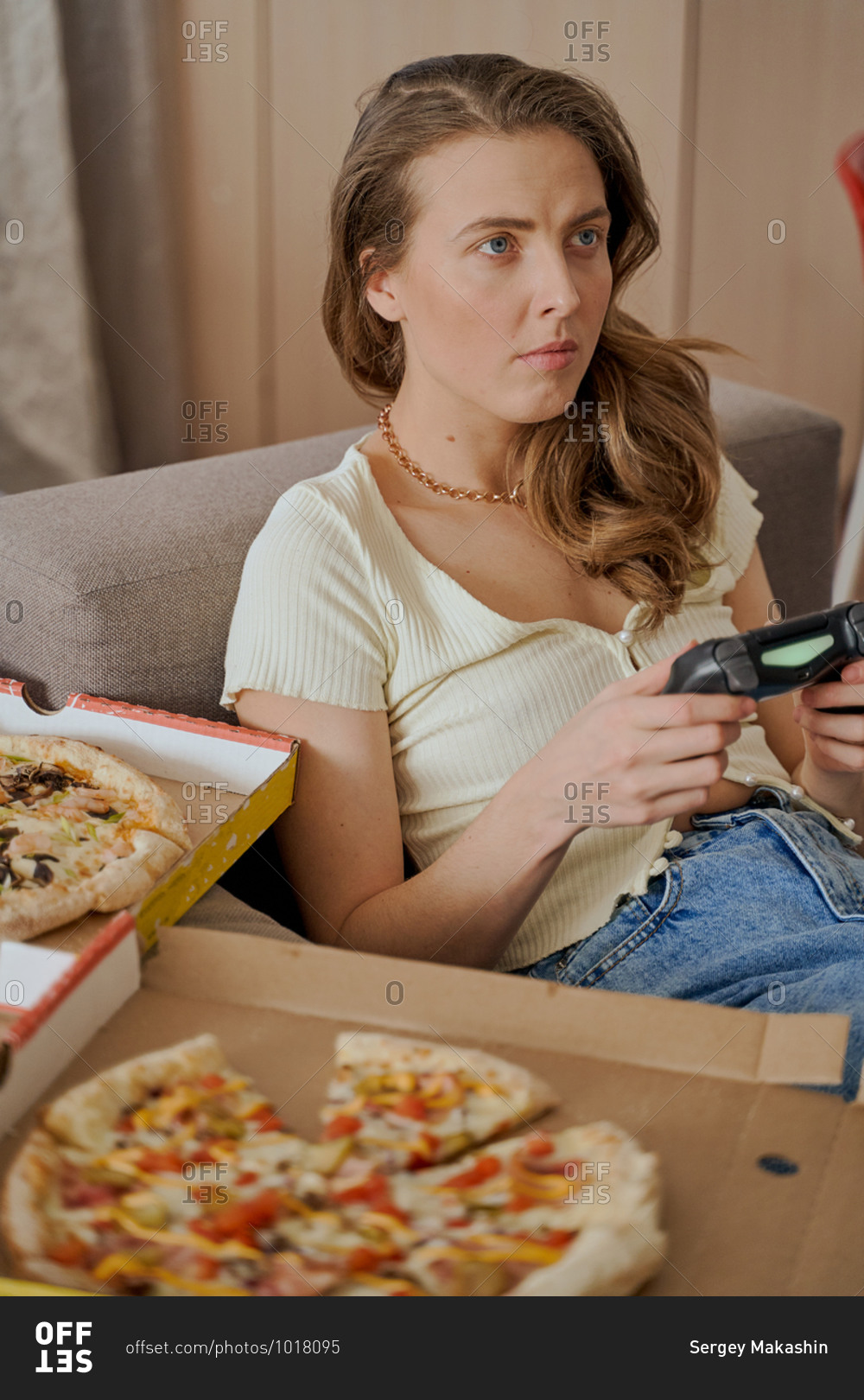 Blonde woman sitting on sofa eating pizza and playing video games
