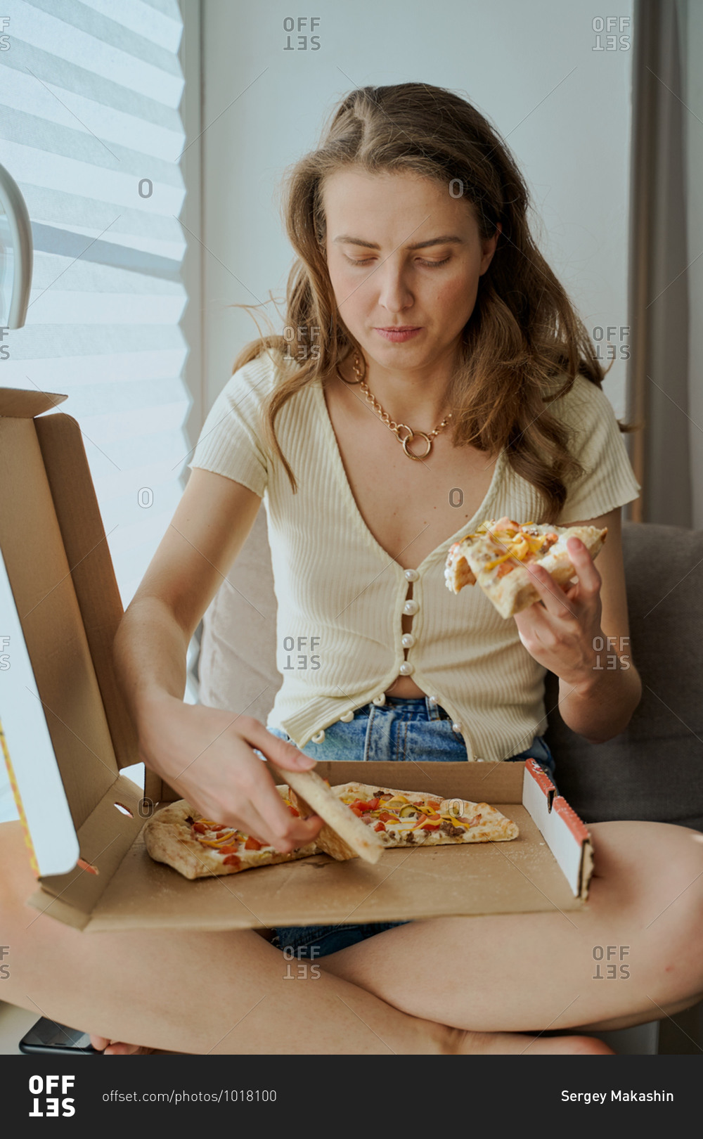 Blonde woman sitting on sofa eating pizza