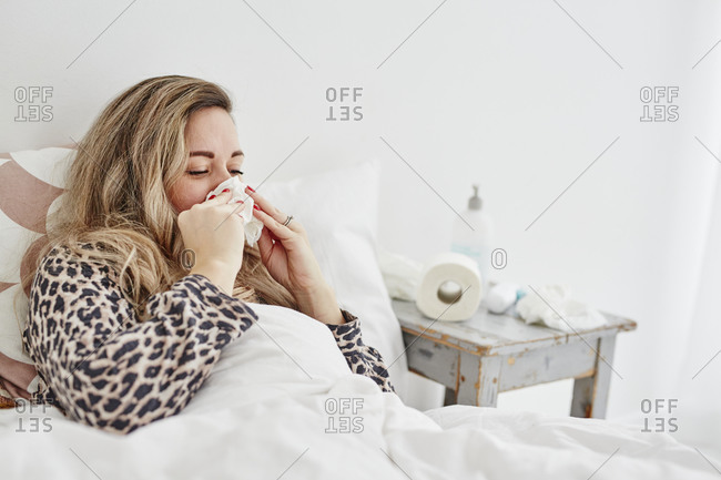Ill woman in bed sneezing