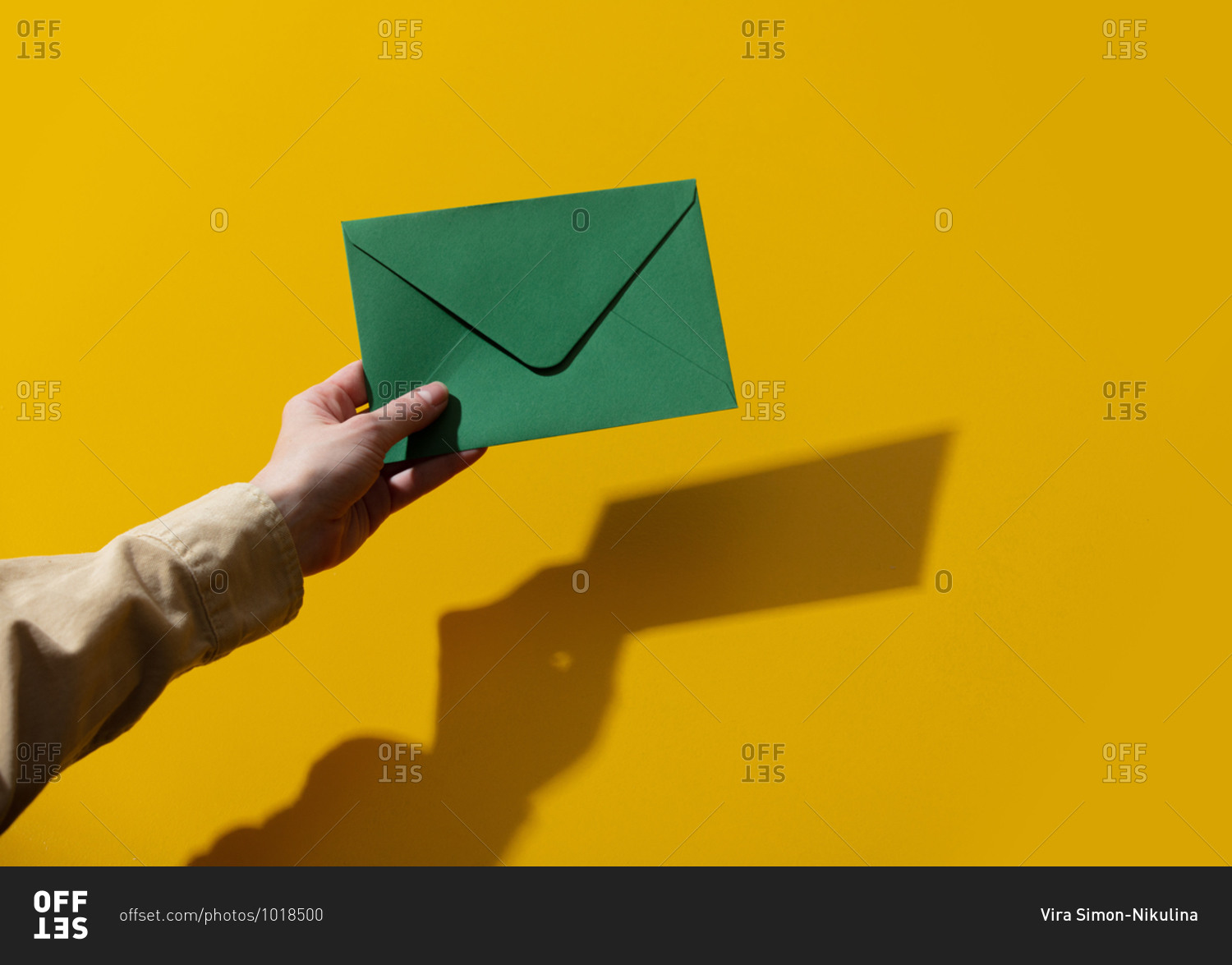 Woman hand holding a green envelope on yellow background