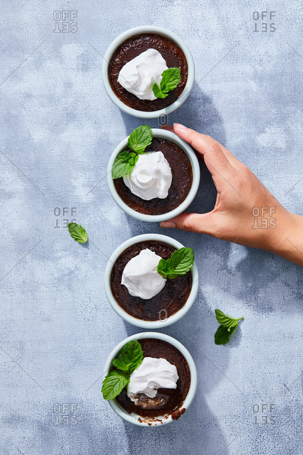 Woman arranging four chocolate mousse dishes with whipped cream and mint on gray surface