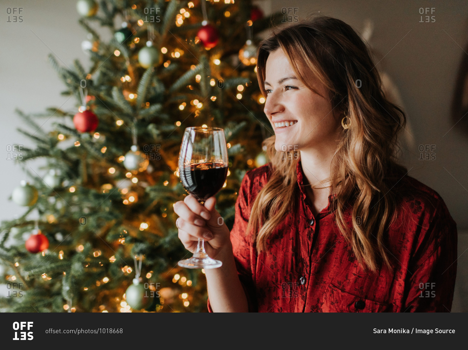 Woman drinking wine beside decorated Christmas tree stock photo - OFFSET