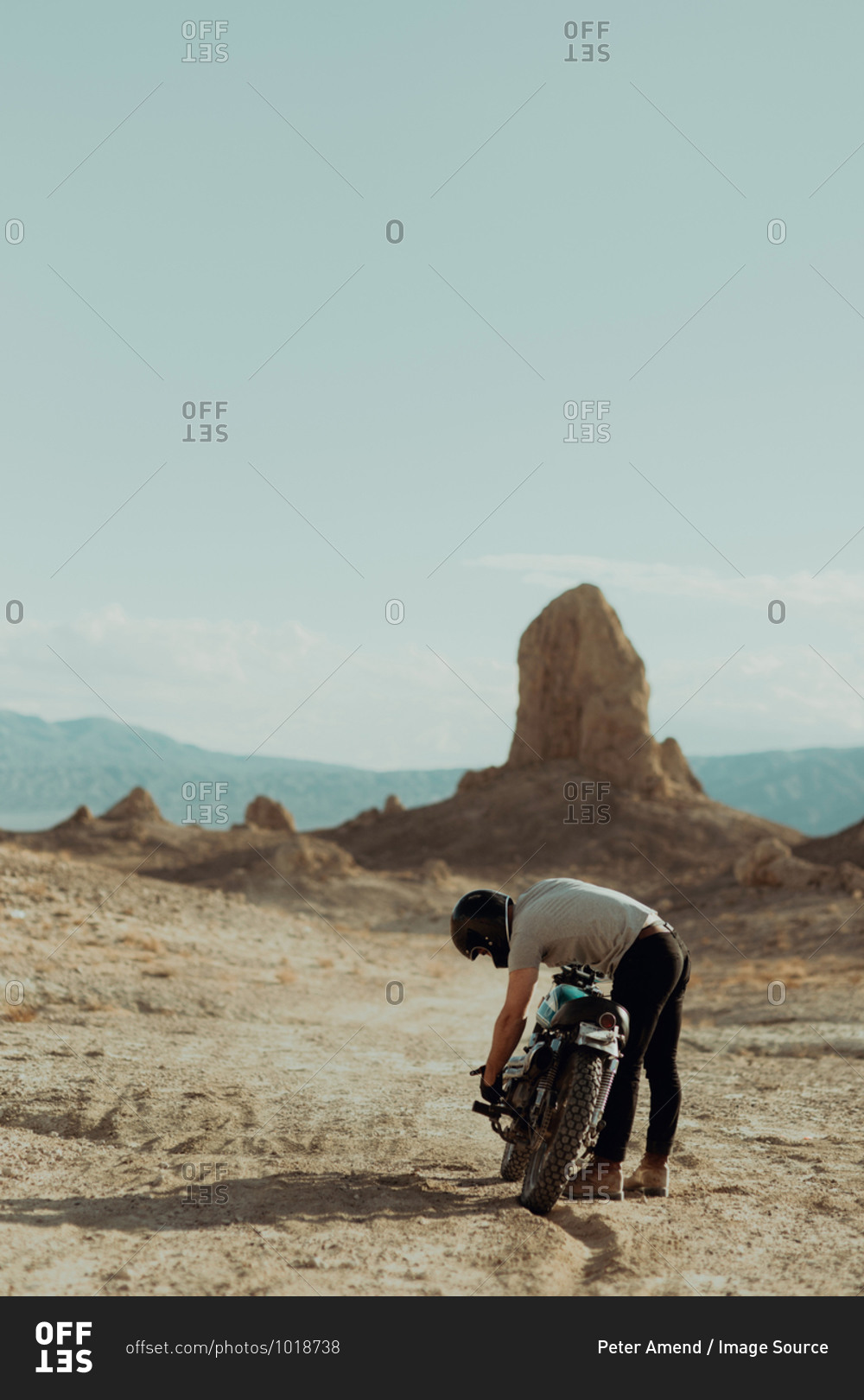 Motorcyclist bending over bike in desert, Trona Pinnacles, California, US