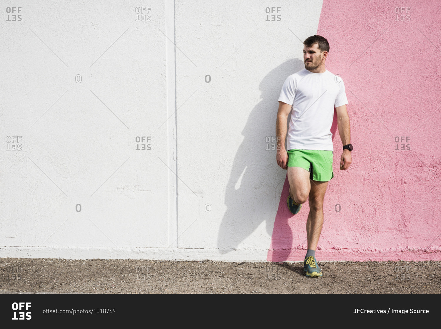 Young male runner leaning against pink and white wall