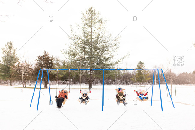 Man and children swinging on row of playground swings in snow