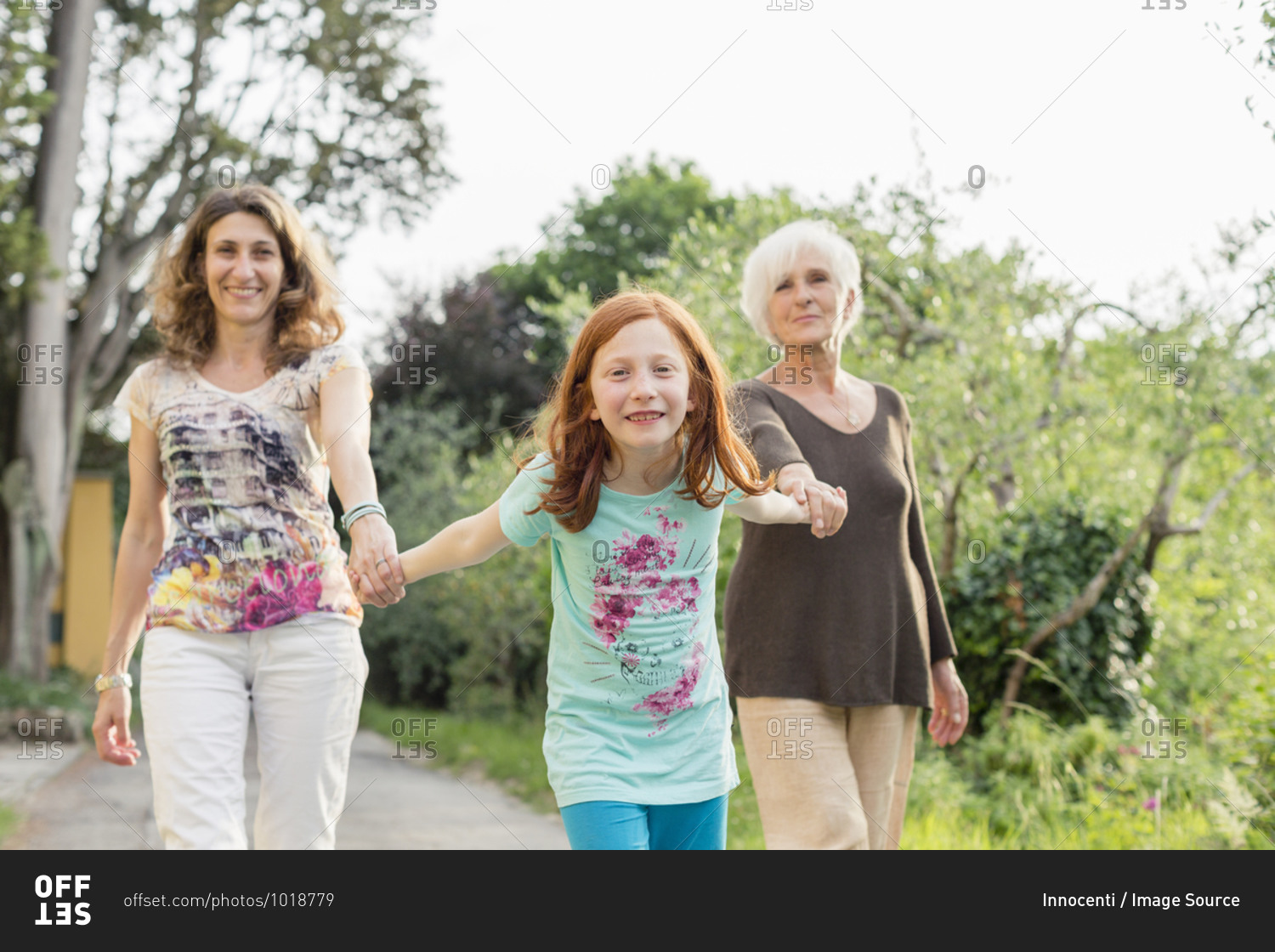 Girl on rural road holding hands with mother and grandmother, portrait