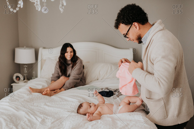 Couple dressing baby daughter on bed in bedroom