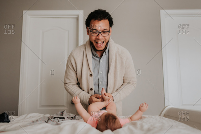 Father dressing baby daughter on bed in bedroom