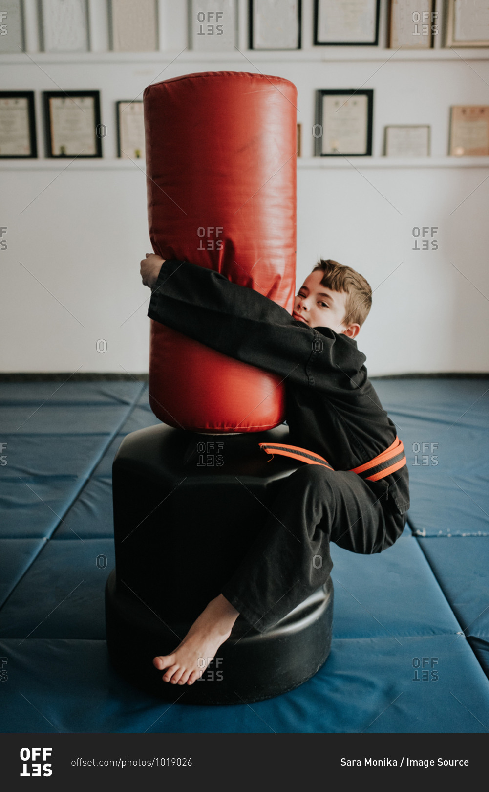 Boy clinging onto punch bag in martial arts studio