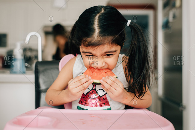 Girl in high chair eating water melon