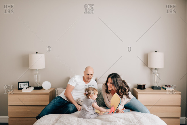 Mother and father on bed with baby daughter looking at story book