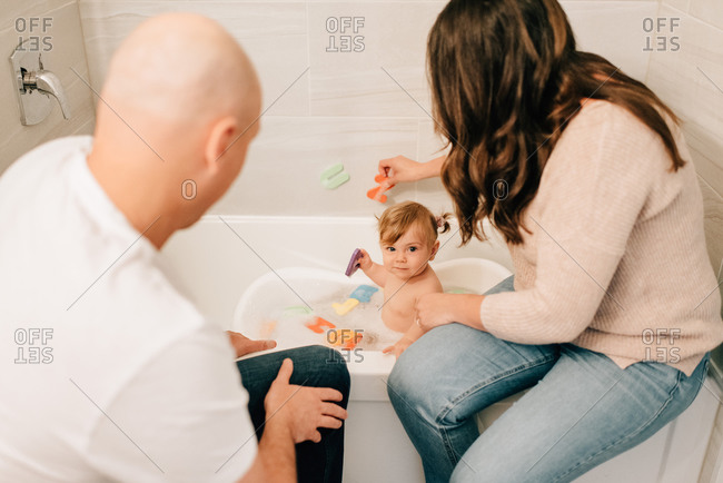 Mother and father playing with baby daughter in bath, over shoulder view