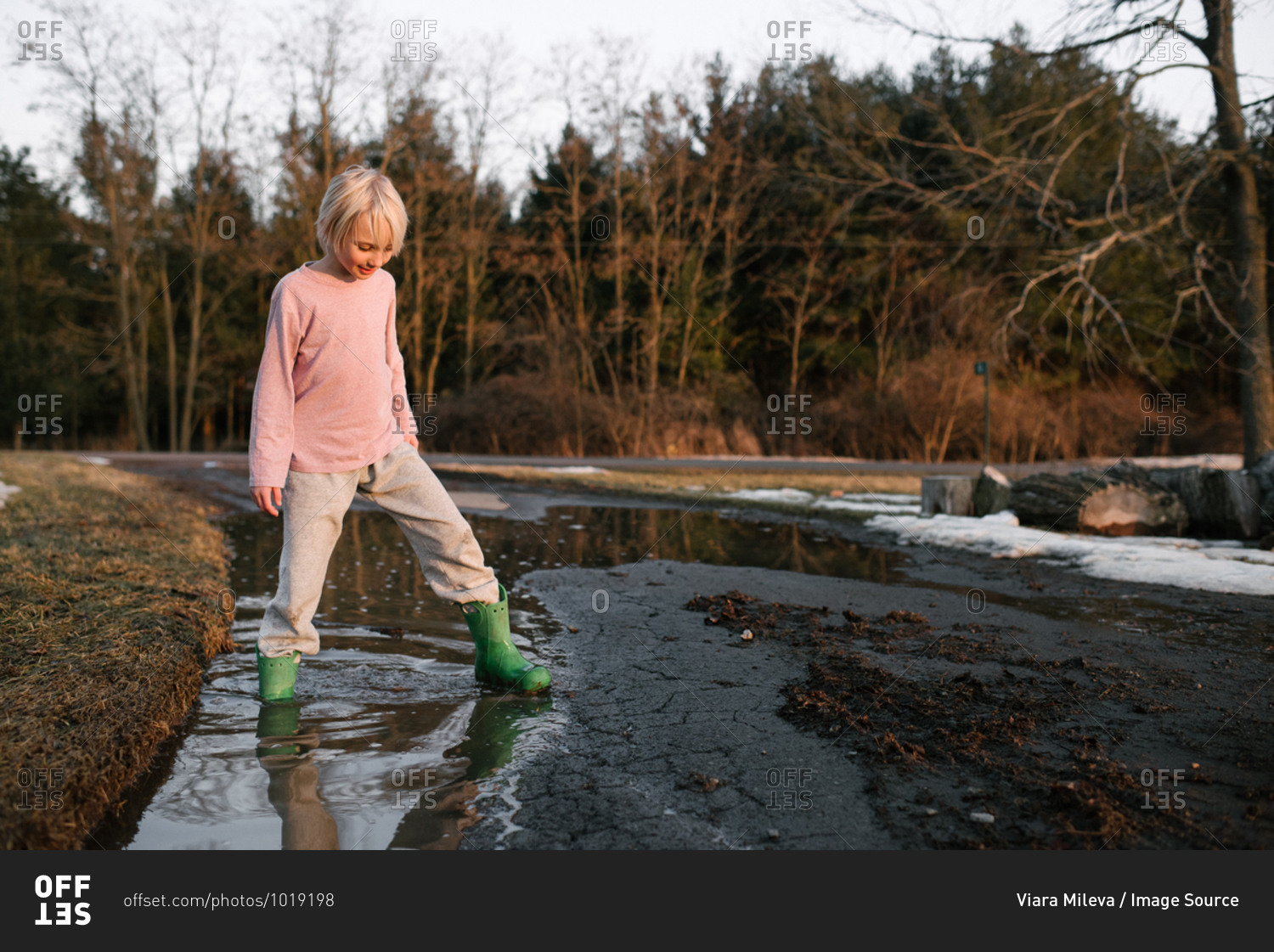 Boy stepping ankle deep in rural meltwater puddle
