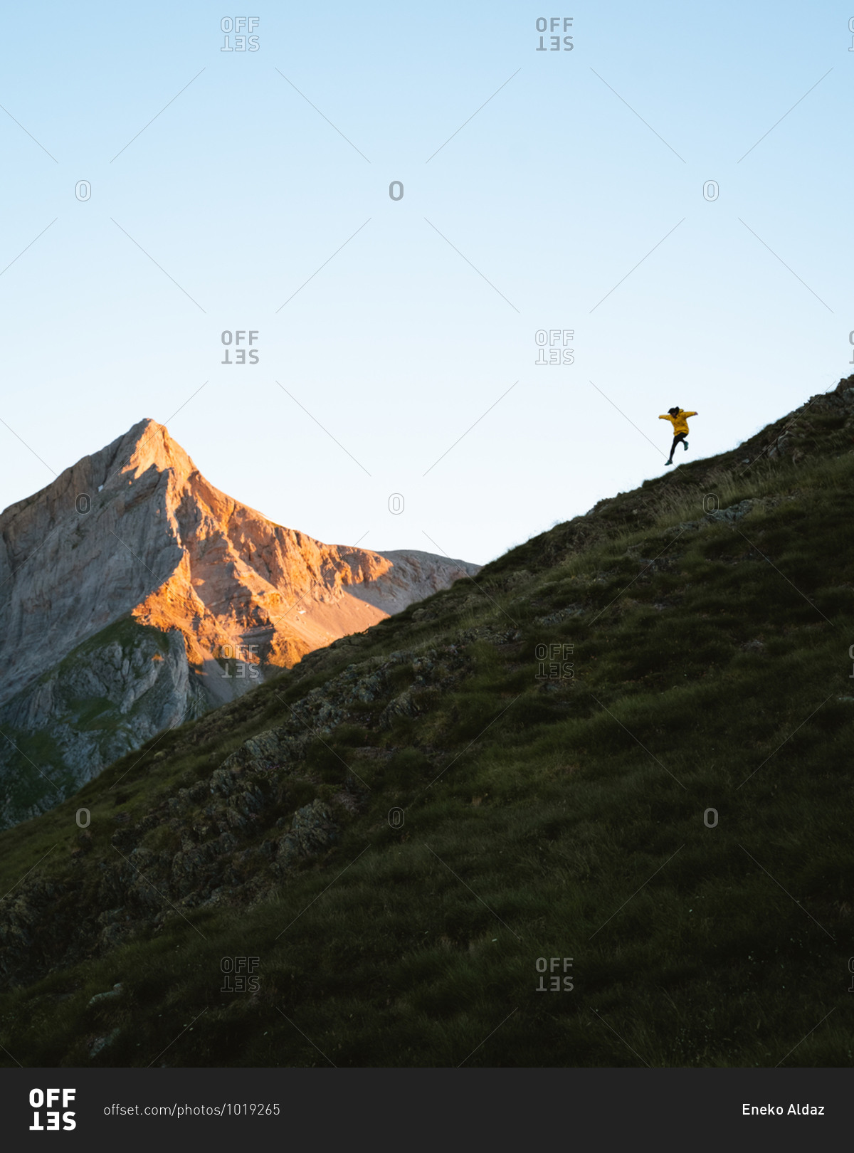 Young man wearing yellow jacket running down a steep hill in Pyrenees