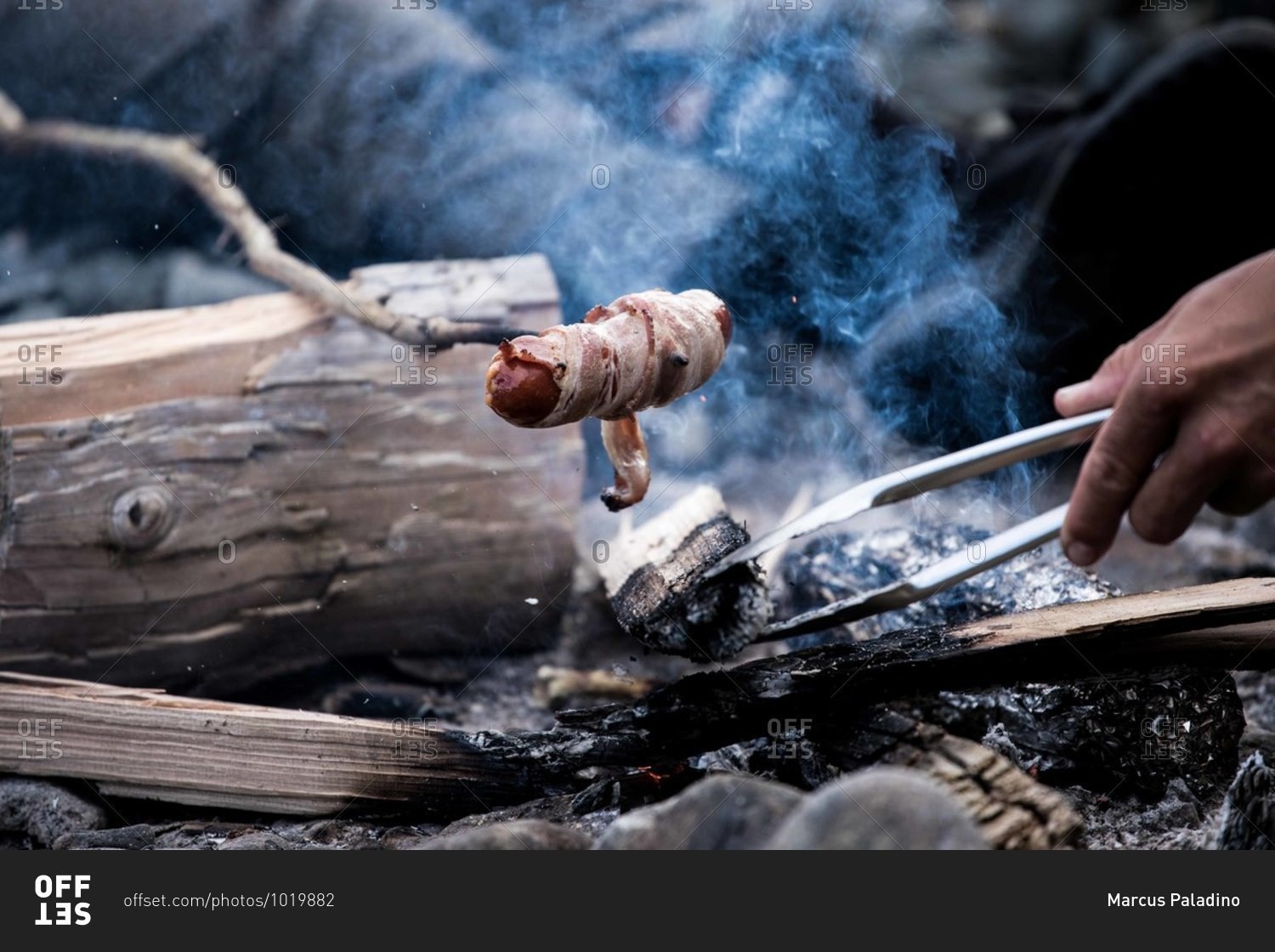 Hot dog wrapped in bacon being cooked over a campfire