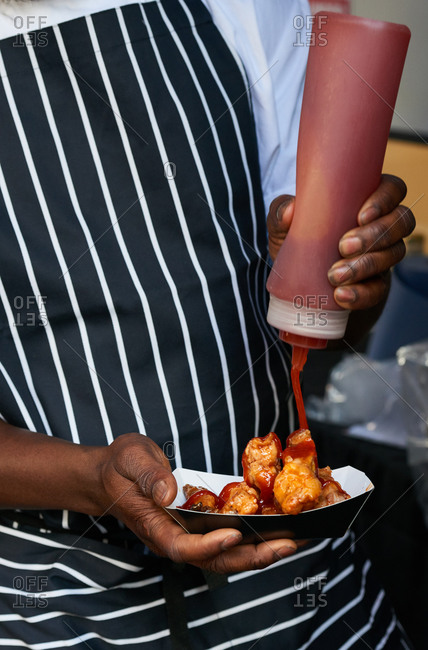 A chef pouring hot chili sauce onto take away fried chicken