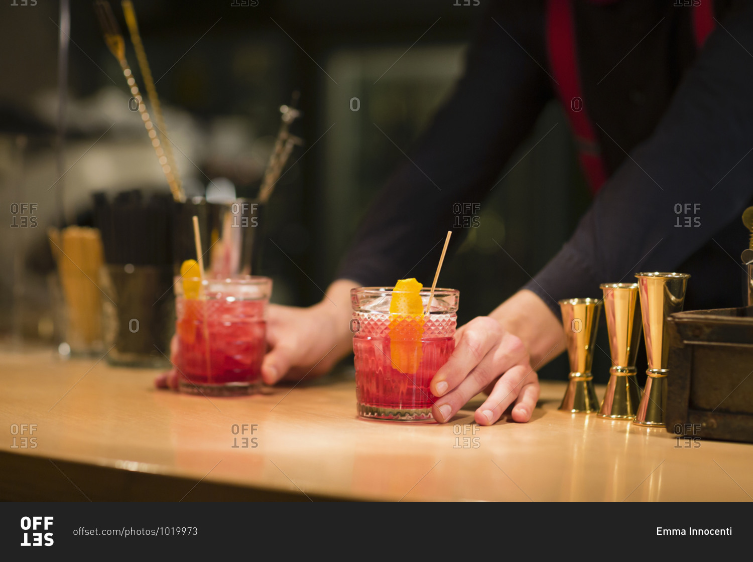 Unrecognizable barman putting glass cups with cold alcohol cocktails on counter while working in restaurant bar
