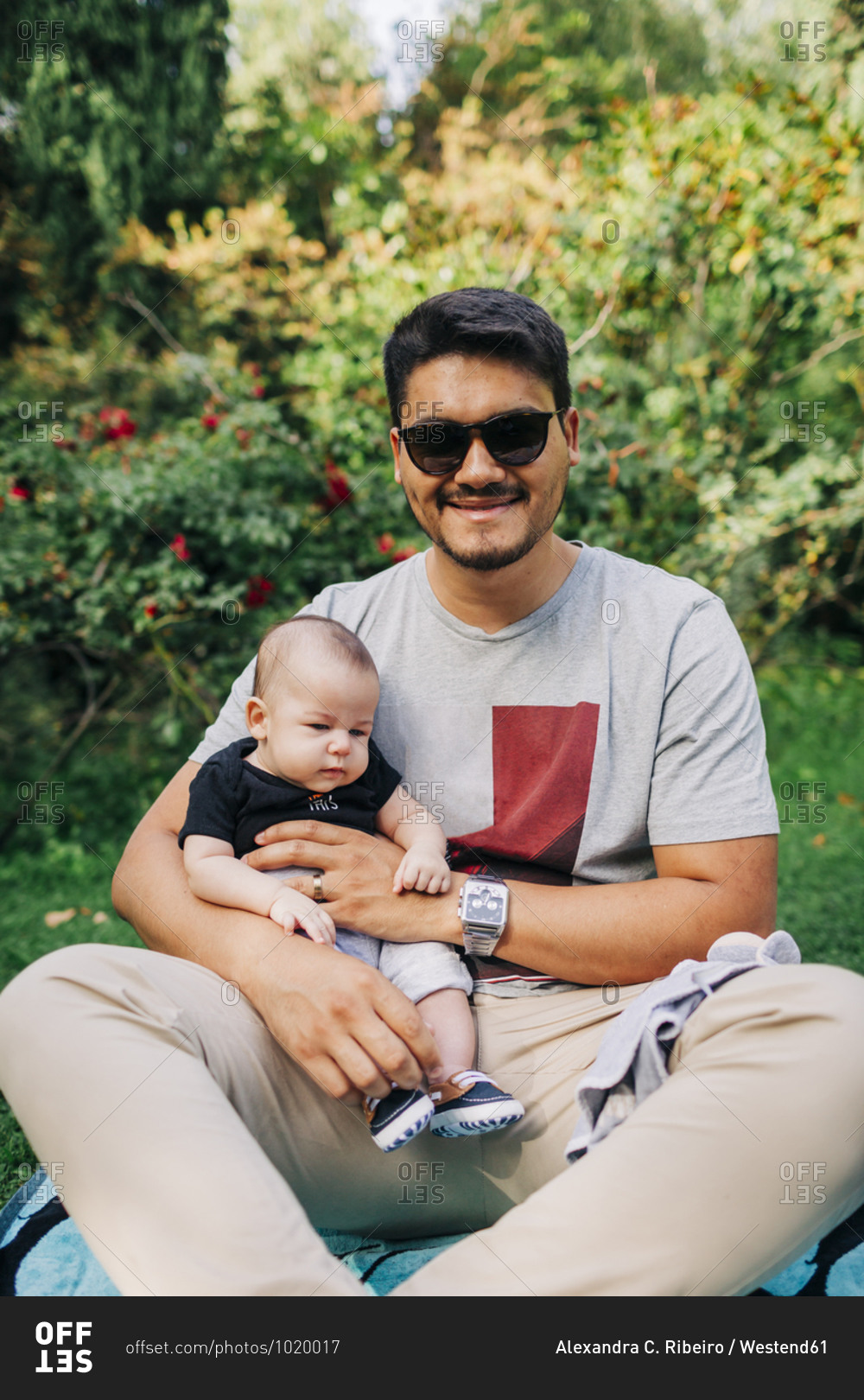 Smiling young man sitting with baby son at park during weekend