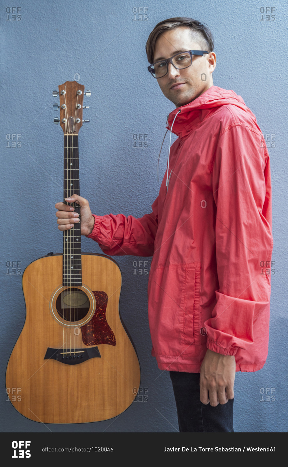 Confident musician holding guitar against blue wall