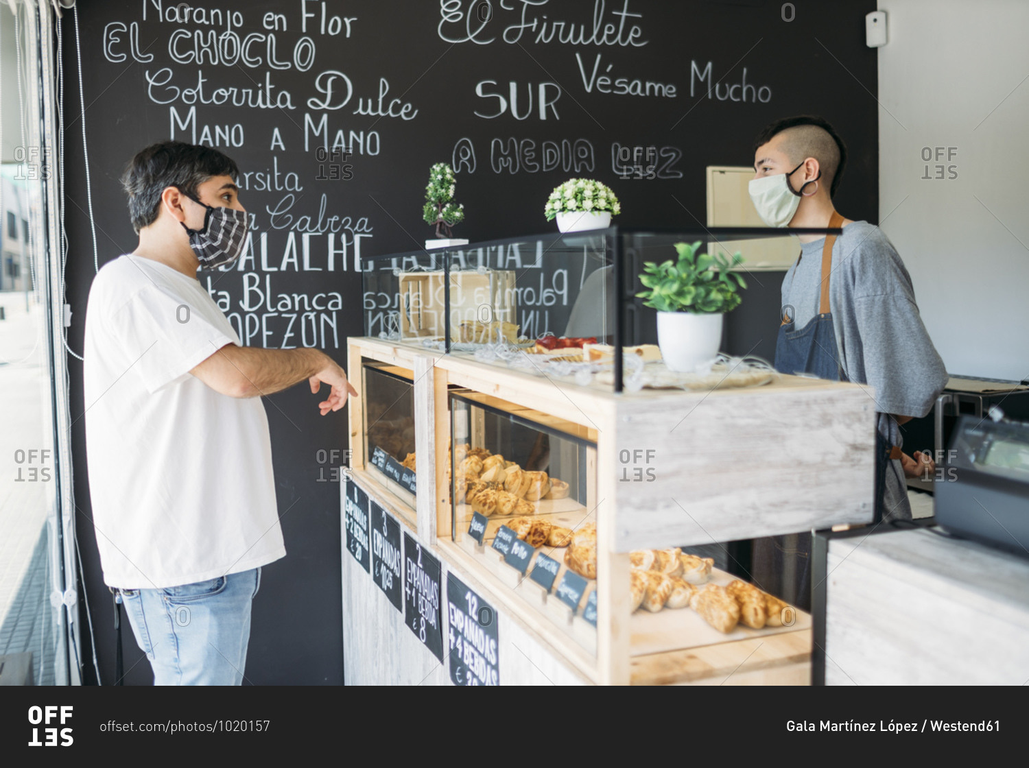 Waiter and customer with protective masks at the counter in a cafe