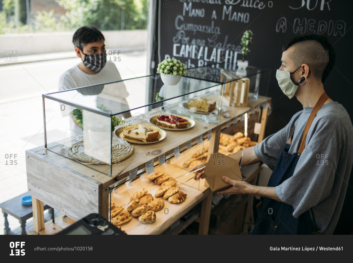 Waiter and customer with protective masks at the counter in a cafe