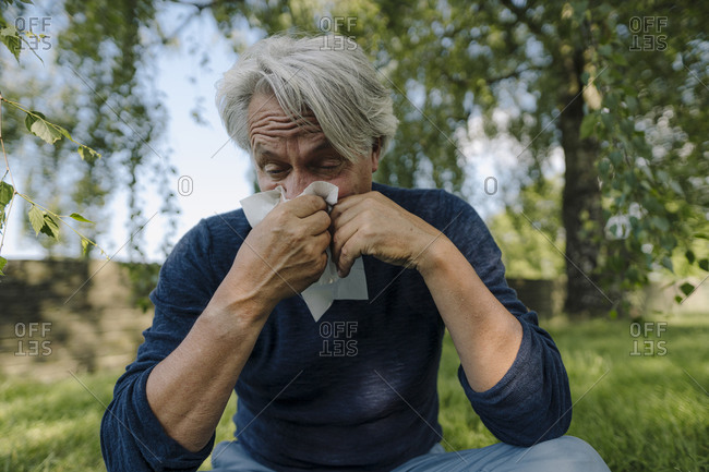 Wrinkled man blowing nose while sitting in field