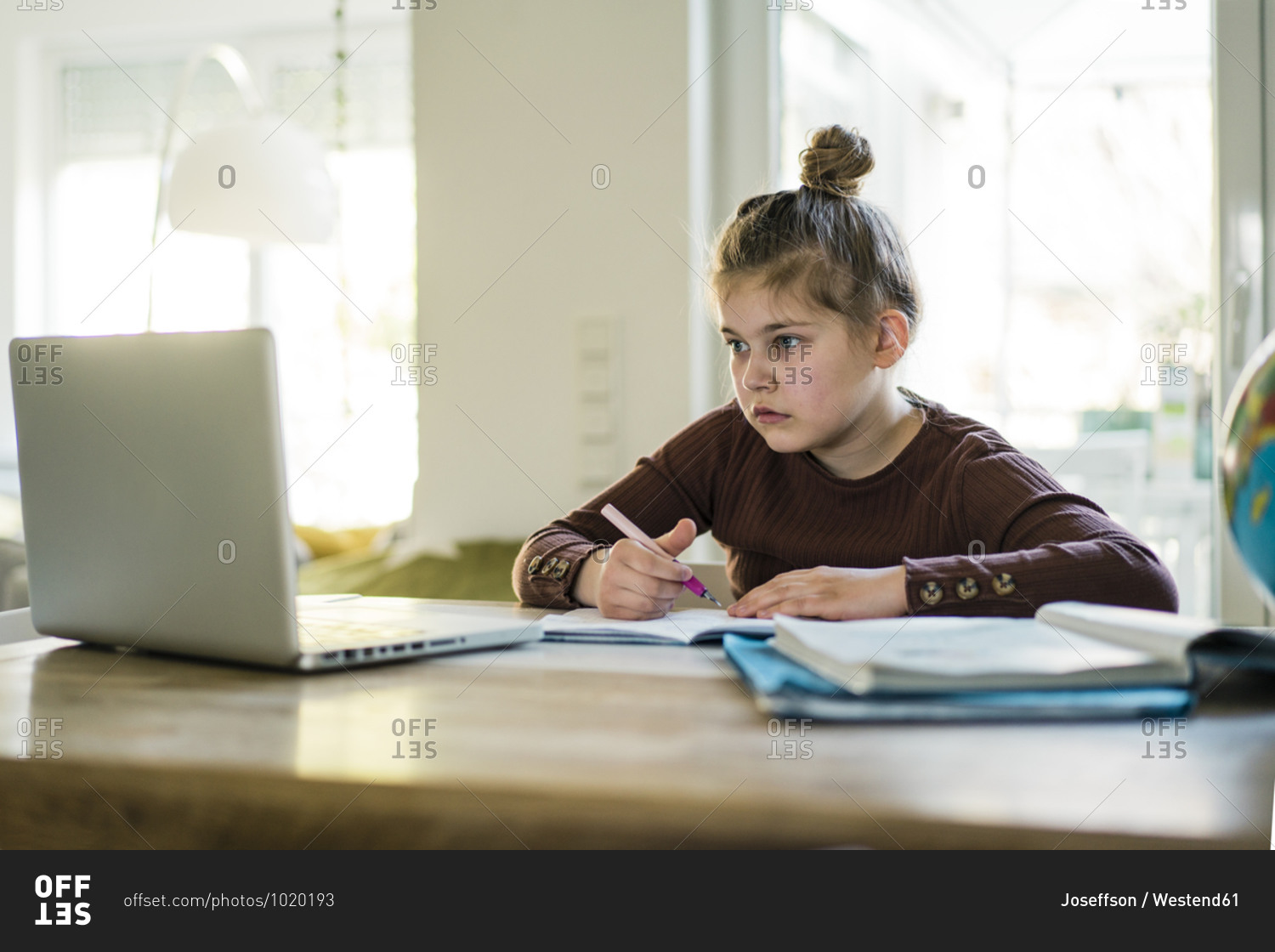 Girl writing in book while studying through laptop at home