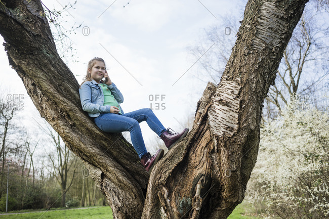 Smiling girl talking on smart phone while leaning over tree trunk in park