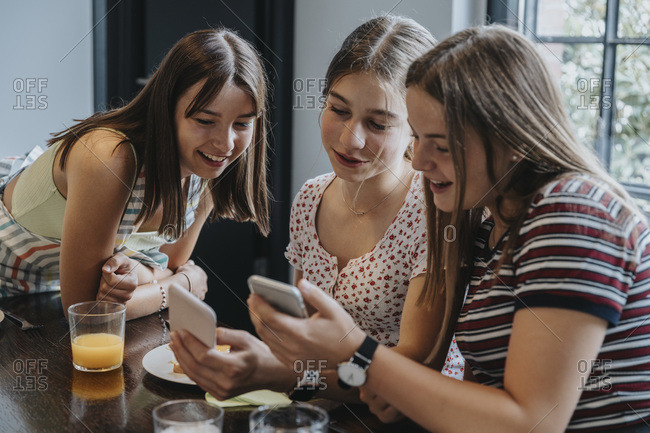 Group of teenage girls meeting for brunch- looking at smartphones